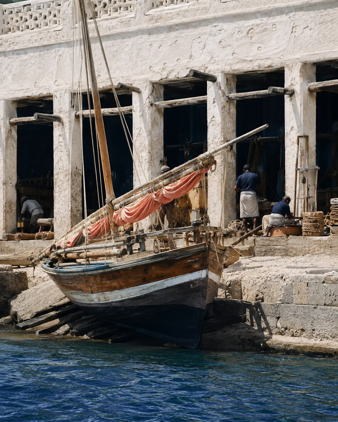 Traditional sailing boat under maintenance beside a waterfront craft workshop