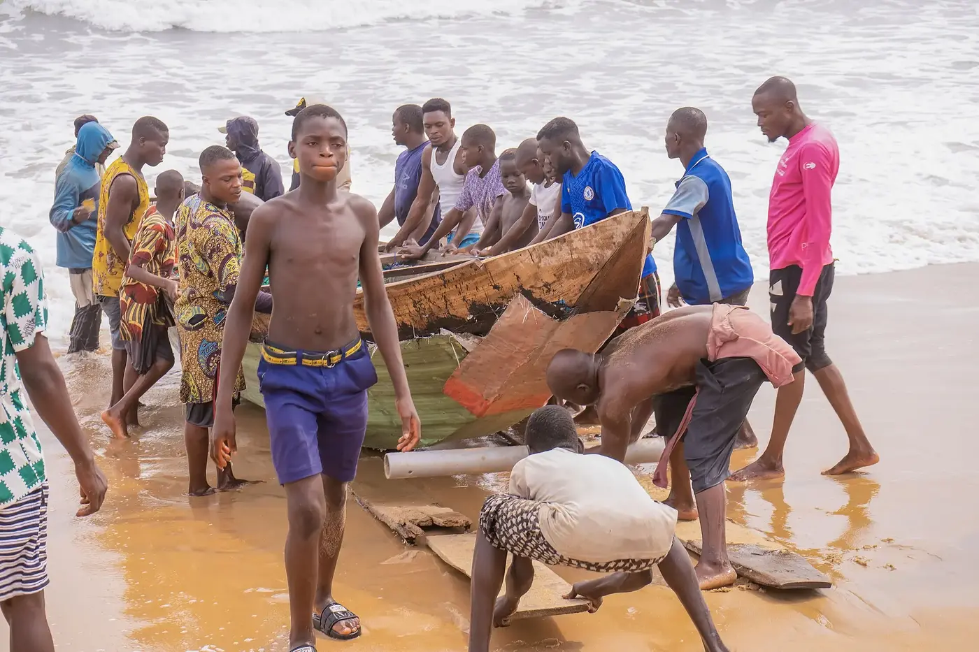 A coastal fishing community bringing a wooden boat ashore in Africa