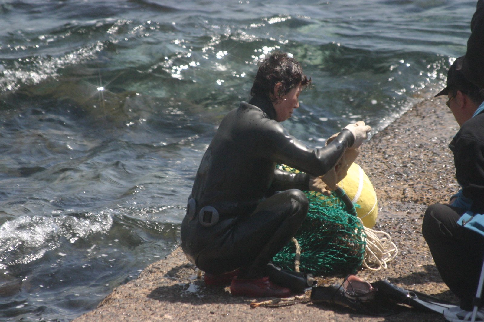 Jeju haenyeo diver in a black wetsuit beside the sea with flotation and net equipment
