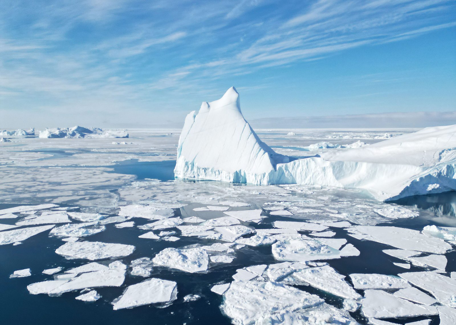Large white icebergs and broken sea ice filling Greenland's Ilulissat Icefjord under a blue sky